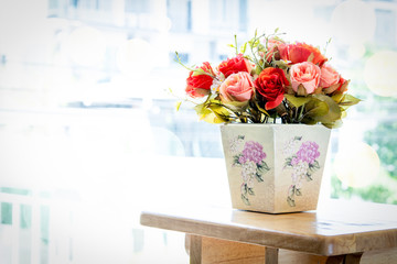 Colorful artificial rose in the vase on wooden table decorating near the window