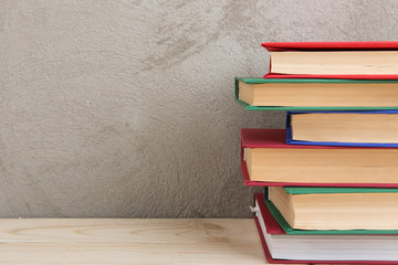 Education and reading concept - group of colorful books on the wooden table, concrete wall blackboard