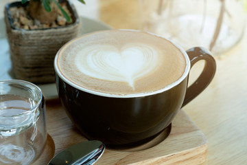 Latte art coffee in the morning time with sunlight on wooden table background at coffee shop.