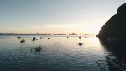 Aerial drone view of boats anchored in the bay with clear and turquoise water on the sunset. Boat and yacht in the tropical lagoon. Tropical landscape. El Nido, Palawan island, Philippines.