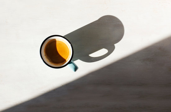  Cup of coffee. Сup of Espresso on a table back lit by the sun casting a long shadow