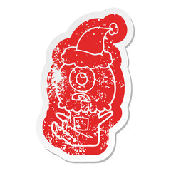 cartoon distressed sticker of a cyclops alien spaceman wearing santa hat