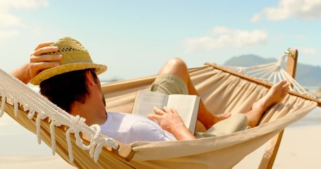 Side view of caucasian man reading in hammock at beach