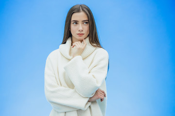 Picture of happy young lady standing on a blue background. Look into the camera. During this time she is dressed in a white warm sweater.