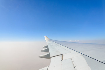 Fototapeta na wymiar Beautiful clear deep blue sky over thick layer of blurry clouds at stratosphere atmosphere viewed from airplane's window located above airplane's wing and jet.
