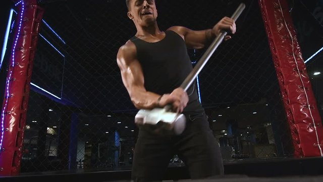 Sport muscular fitness man hitting wheel tire with hammer sledge in gym strong man fitness and bodybuilding training workout fitness concept 