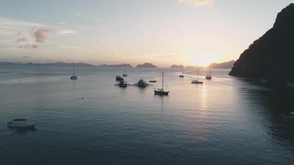 Aerial drone view of boats anchored in the bay with clear and turquoise water on the sunset. Boat and yacht in the tropical lagoon. Tropical landscape. El Nido, Palawan island, Philippines.