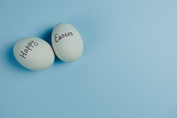 Happy Easter text on white eggs isolaed on blue background. Easter holiday concept. Flat lay. Top view