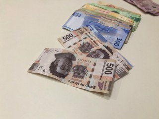 Many mixed Mexican peso bills spread over a beige desk