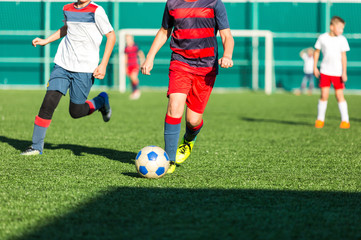 Boys in red white sportswear running on soccer field. Young footballers dribble and kick football ball in game. Training, active lifestyle, sport, children activity concept 