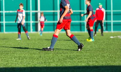 Boys in red white sportswear running on soccer field. Young footballers dribble and kick football ball in game. Training, active lifestyle, sport, children activity concept 