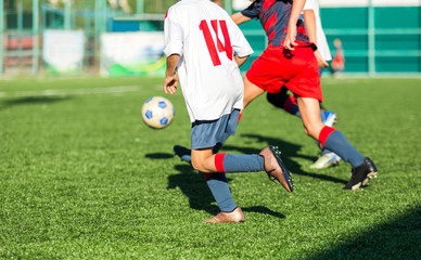Obraz premium Boys in red white sportswear running on soccer field. Young footballers dribble and kick football ball in game. Training, active lifestyle, sport, children activity concept 