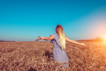 A girl in a dress, standing in wheat field in the summer, arms outstretched to the side, the farm and spikelets of wheat rest on nature.