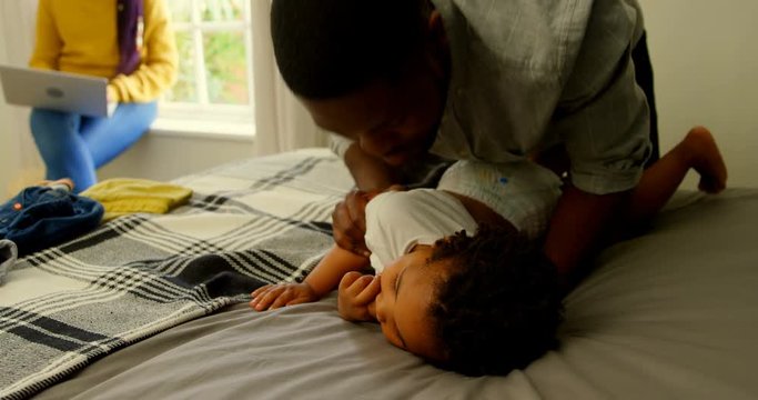Front view of black father helping his son changing his clothes on bed in a comfortable home 4k