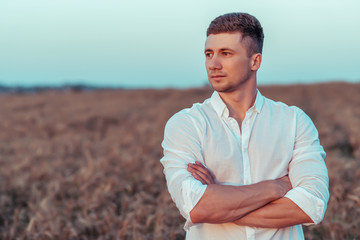 A young man in a white shirt, in the summer on wheat field, looks into the distance. Free space for...