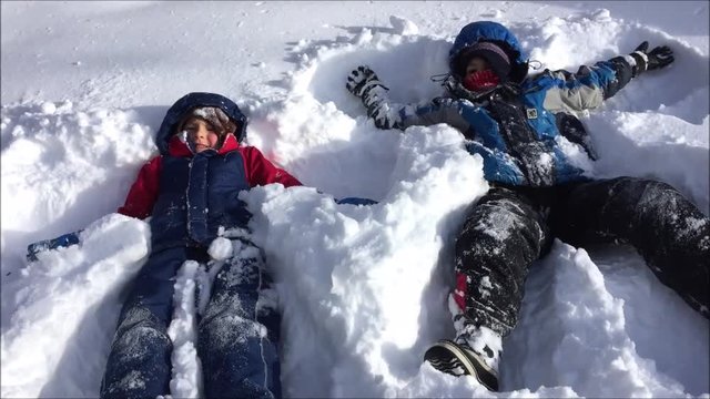 Two children playing in heavy snow in a city playground in Canada and making snow angels during a cold Canadian winter