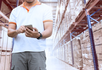 Young man with smartphone with contact to customer in warehouse background.