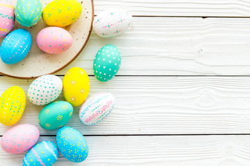 Festive Easter table. Colorful Easter eggs on plate on white wooden background top view space for text