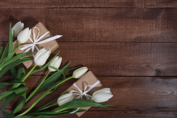 White tulips and gift boxes on brown wooden table. Women day concept. White ribbon, craft wrap, 8 march, spring