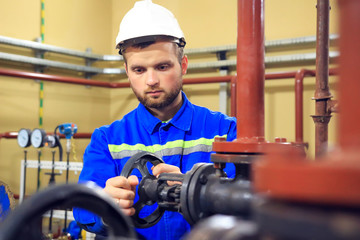 Worker turning gate valve on boiler pipe