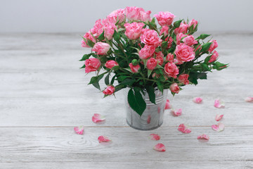 Bunch of roses in tin bucket and petals on white wooden table. Women day concept. Spring, blooming, 8 march, birthday