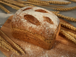 tasty, fragrant bread, whole loaf on a wooden board with ears of corn and grains