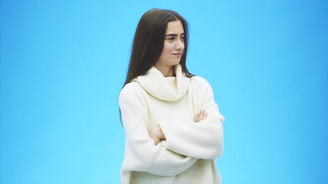 Beautiful young girl standing on a blue background. During this time she is dressed in a white sweater. With long black hair.