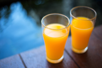 Two glasses of orange juice are placed on the wooden floor near the pool.