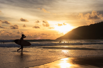 silhouette of man with surfboard on the beach at sunset