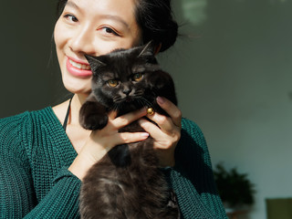Portrait of beautiful Chinese young girl hug her cute British Shorthair Cat who has amazing orange eyes at home and smile at camera in sunny afternoon, happy pets owner lifestyle.