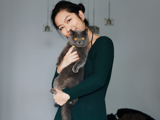 Portrait of beautiful Chinese young girl hug her cute British Shorthair Cat who has amazing orange eyes at home and smile at camera in sunny afternoon, happy pets owner lifestyle.