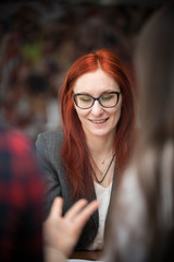 A business conference. A ginger woman in glasses looking down and smiling