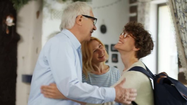 Medium shot of Caucasian woman with short curly hair entering apartment of her relatives and embracing them