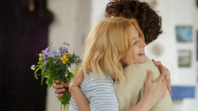 Medium shot of blonde middle-aged woman embracing young woman giving her small bouquet of flowers