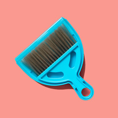 A pale blue dustpan and brush lying on living coral background. In the style of pop art. Top view.