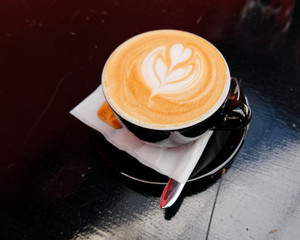 art cappuccino coffee with heart shaped tree in black cup on dark background