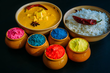 Holi indian festival of colors. Food with colours, steam rice, panir butter masala, pepper chilie, starnise. Powder colours arranged over black background. Selective focus