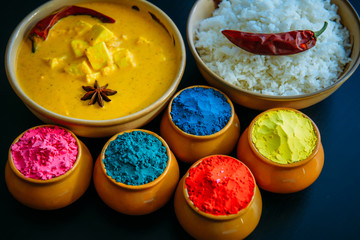 Holi indian festival of colors. Food with colours, steam rice, panir butter masala, pepper chilie, starnise. Powder colours arranged over black background. Selective focus