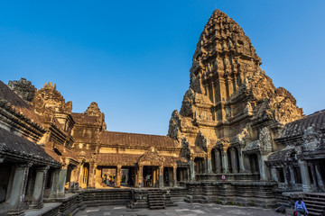 Angkor Wat, Cambodia - February, 2019:  Tourists explorelotus bud shaped principal tower with paved courts and covered galleries in Angkor Wat temple in golden sunset light