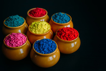 Colorful Holi powder in cups closeup. Bright colours for Indian holi festival in clay pots. Selective focus. Black background, top view