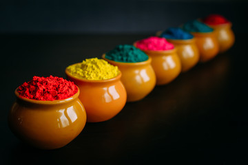 Line of colorful Holi powder in cups closeup. Bright colours for Indian holi festival in clay pots....