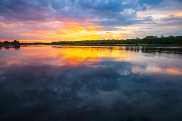 Fototapeta na wymiar Scenic beautiful orange sunset among heavy clouds on the horizon above the river