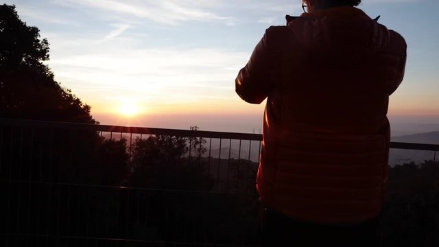 Back view of a man taking pictures at sunrise