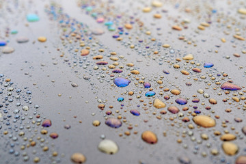 drops of water mixed with bitumen on the dark surface shimmer with all the colors