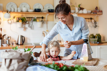 Family are cooking italian pizza in cozy home kitchen. Happy mother is teaching cute kid to prepare food or meal for Thanksgiving dinner. Little girl is helping woman. Children chef concept.