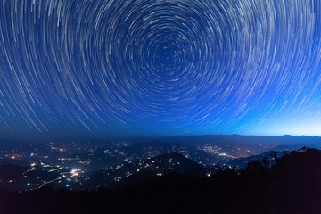 Night sky star trails around the North star with city lights in the background taken from the top of a hill in himalayas - 253239802