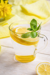 Glass of water with lemon and mint on light wooden table with yellow cloth. 
