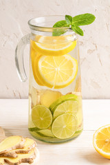 Glass decanter with water, infused with lemon, lime and ginger on light background. 