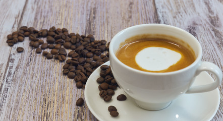 white cup with black coffee with milk. Handful of coffee beans on a wooden table. horizontal view of a cup with a coffee drink. Copy space close up.