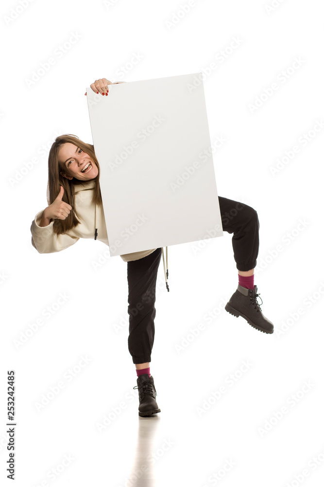 Wall mural Young model in hoodie holding an empty advertising board on white background - Wall murals